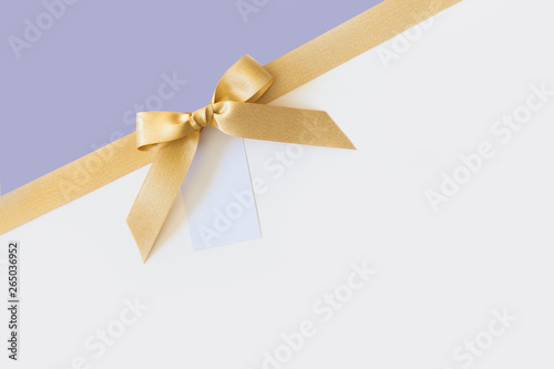 Gold ribbon with a bow as a gift on a white and lavender background