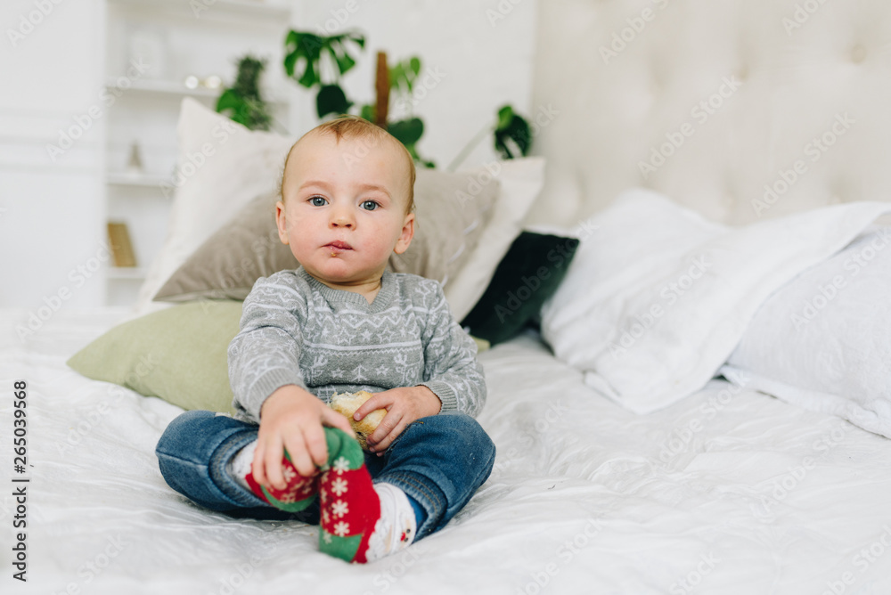 Naklejka premium Cute little toddler boy sitting on bed holding a snack looking straight