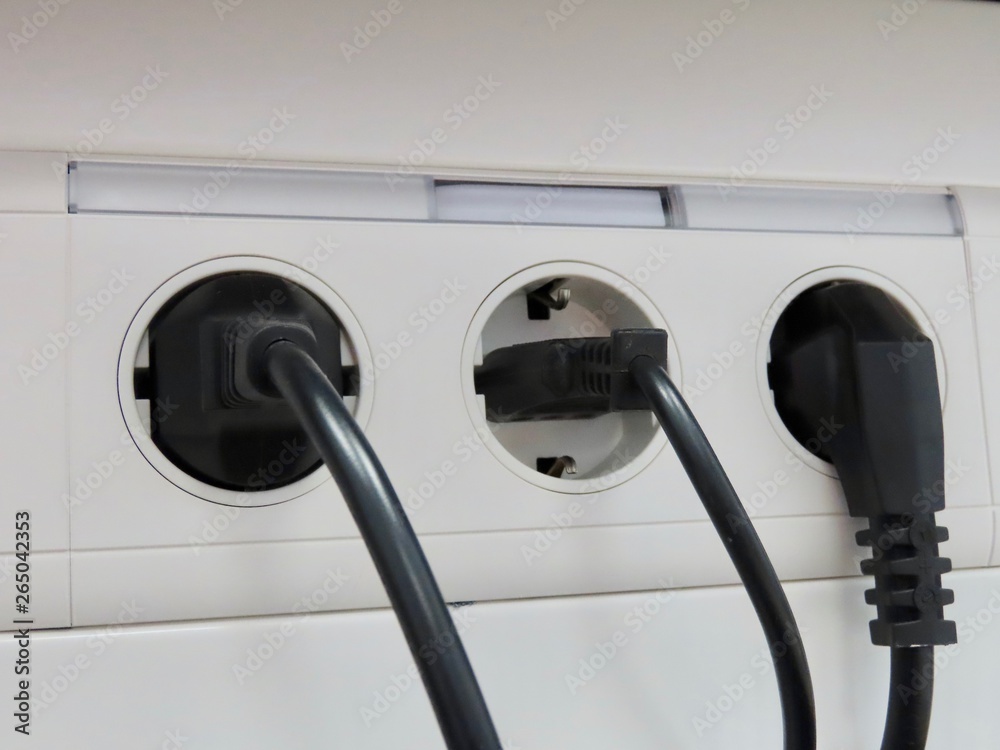 Three differently shaped black European AC power plugs in white block of sockets Three differently shaped black European AC power plugs in white block of sockets
