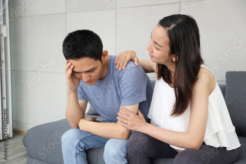 young pregnant wife comforting and touching shoulder young husband while sitting on sofa