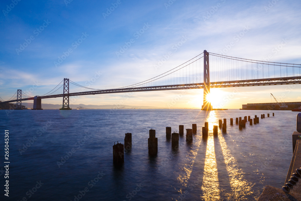 San Francisco Bay Bridge with light beams illuminating the blue waters at sunrise