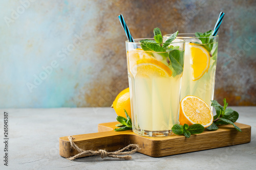 Murais de parede Two glass with lemonade or mojito cocktail with lemon and mint, cold refreshing drink or beverage with ice on rustic blue background