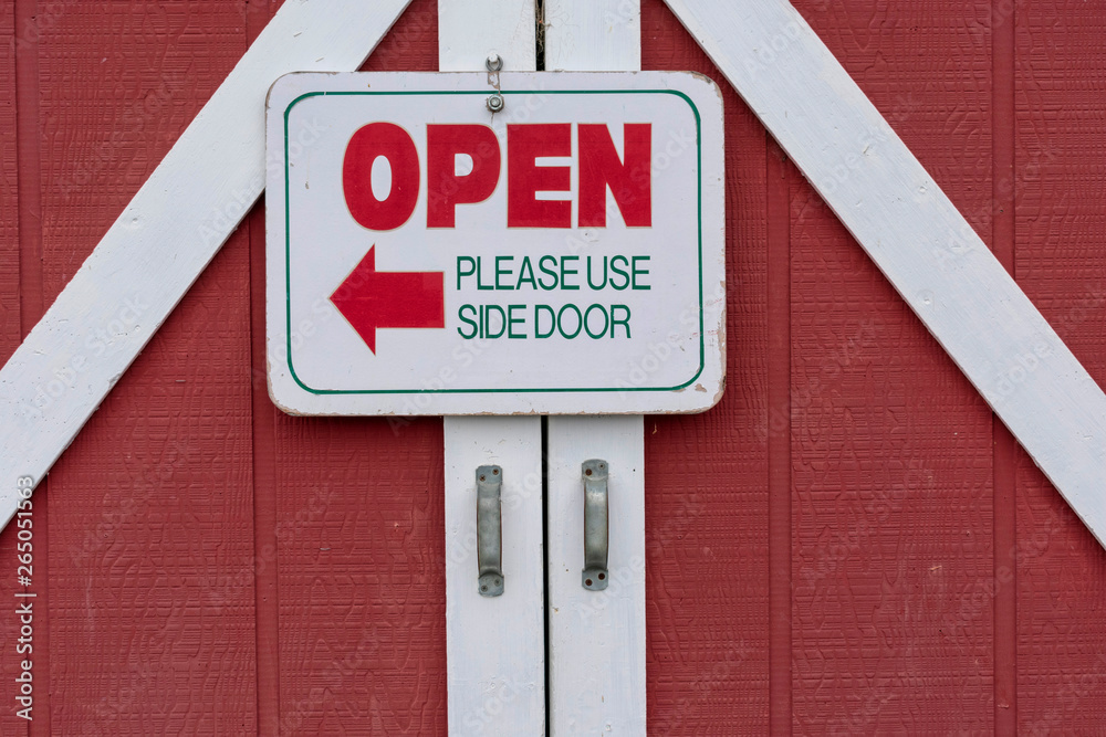 Fototapeta premium Red barn door with the sign : open please use side door
