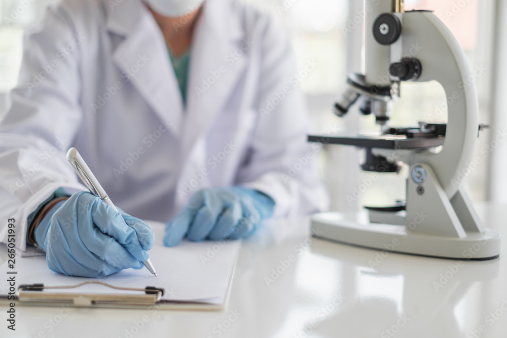 A scientist hands writing on a clipboard in laboratory with test tube microscope and solutions. A scientist hands writing on a clipboard in laboratory with test tube microscope and solutions.