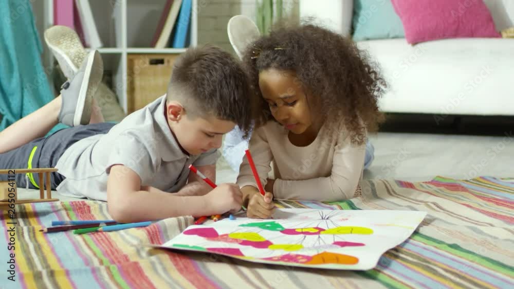 Little african girl and caucasian boy lying together on floor in kids room, talking and drawing greeting poster for Mothers Day Little african girl and caucasian boy lying together on floor in kids room, talking and drawing greeting poster for Mothers Day