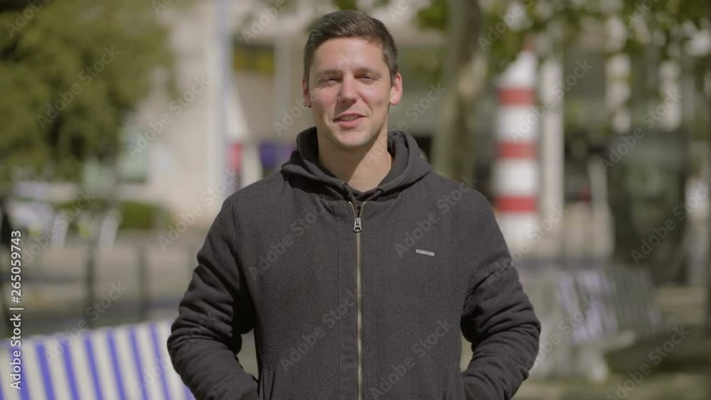 Handsome young man talking at camera outdoor. Front view of happy young man with hands in pockets and crossed arms talking and smiling at camera on street. Emotion concept Handsome young man talking at camera outdoor. Front view of happy young man with hands in pockets and crossed arms talking and smiling at camera on street. Emotion concept