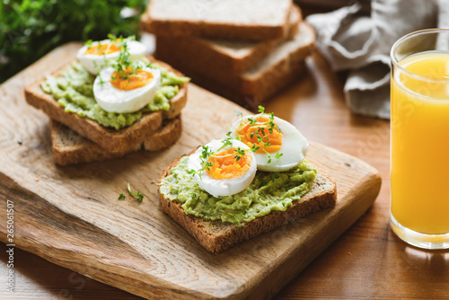 Toasts with avocado, egg, micro greens and glass of orange juice on wooden table. Healthy useful breakfast