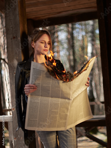 Young woman in a leather jacket checkered pants and white sneakers with a burning newspaper in her hands.