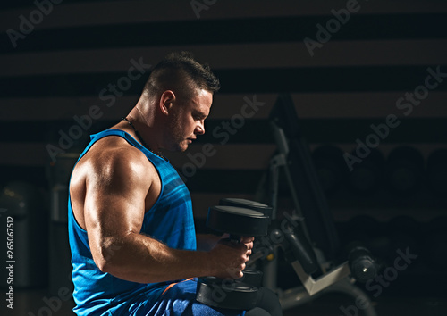 Strong healthy bodybuilder doing weightlifting exercise in fitness club