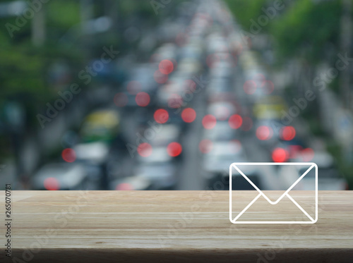 email flat icon on wooden table over blur of rush hour road with cars in city, Contact us concept