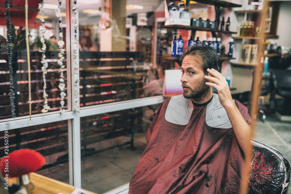 Haircut hair salon man looking in mirror at his hairstyle after barber cut with scissors. Male beauty men care lifestyle.