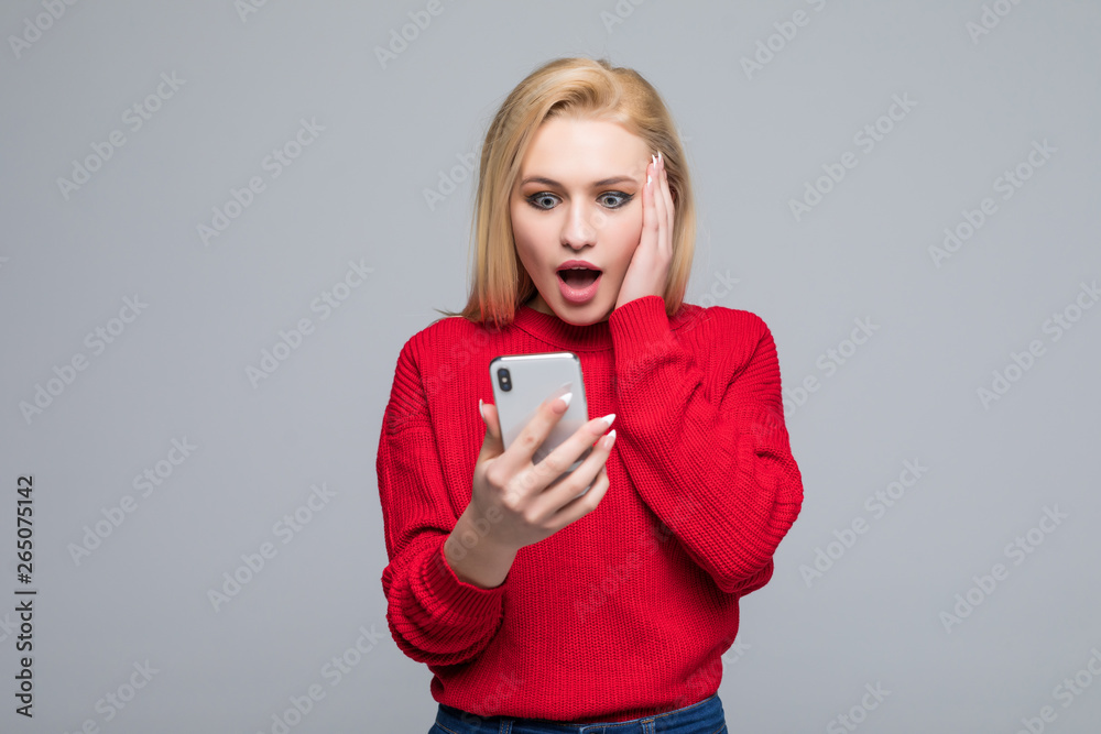 Portrait amazed young girl looking at phone isolated on gray wall background. Human reaction Portrait amazed young girl looking at phone isolated on gray wall background. Human reaction