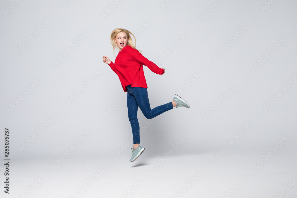 Fototapeta premium Full length portrait of a joyful young woman jumping and celebrating over gray background