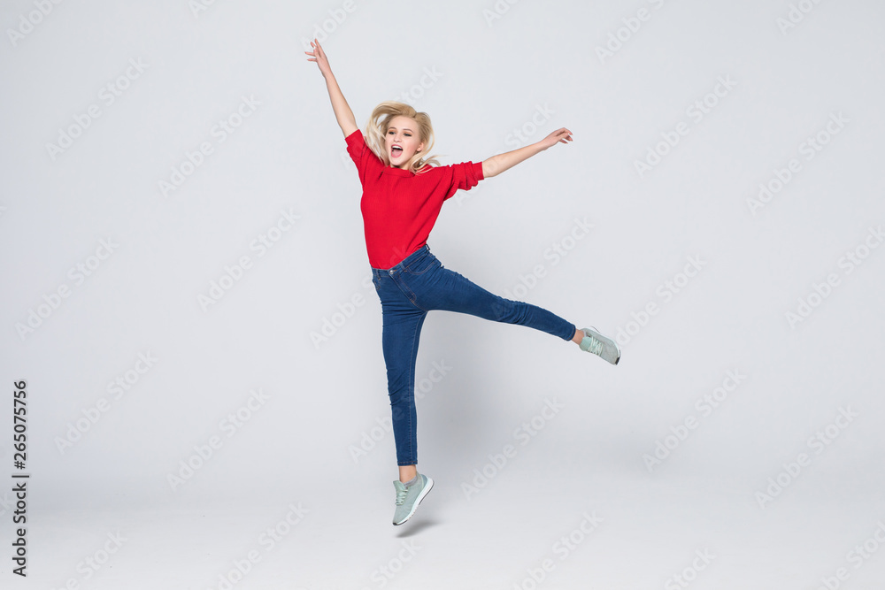Full length portrait of woman wearing jeans and t-shirt jumping and rejoicing with perfect smile isolated over gray background Full length portrait of woman wearing jeans and t-shirt jumping and rejoicing with perfect smile isolated over gray background
