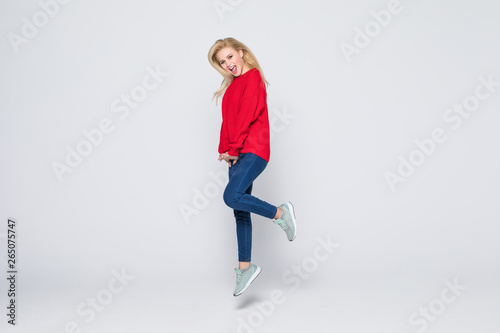 Full length portrait of a joyful young woman jumping and celebrating over gray background