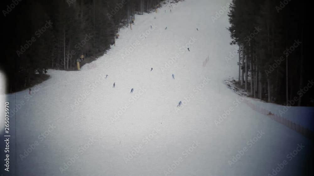 Fake 8mm film projection: many skiers making a descent from a ski slope at different speeds. Long handheld shot. Winter sports, fun, active people.