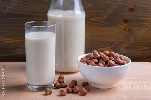 Glass of Hazelnut milk and bottle and organic hazelnuts on wooden background  Alternative Milk. Nuts milk