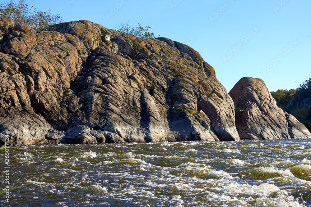 Сliffs on the banks of the mountain river with rapids flowing along rocky banks in wilderness at autumn. Waves, spray, foam and crag.