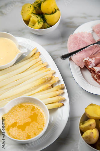 Platte weißer Spargel mit Sauce Hollandaise, zerlassener Butter, Kochschinken, geräucherten Schinken und Kartoffeln auf Marmor Hintergrund