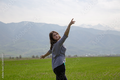 Young beautiful girl in nature. Good mood on a bright spring day. Green fields and blue mountains. Tourism and travel.