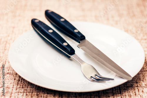 White empty plate with knife and fork on wooden background .
