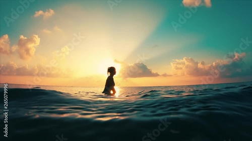 Young causasian woman surfer sits on the line up during morning surf session, waits her wave and enjoys warm tropical sunrise photo