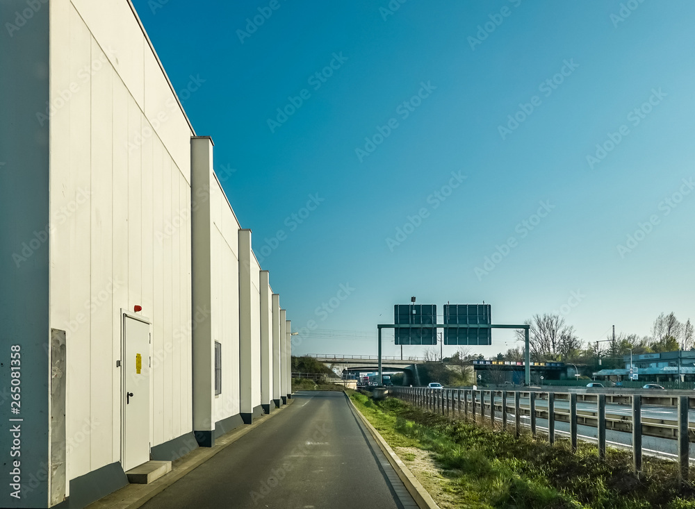 View of an ugly windowless warehouse from an asphalt road next to a motorway in Germany