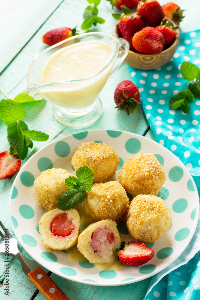 Cottage cheese dumplings with fresh strawberry, served with sour-honey sauce, delicious summer dessert on the kitchen wooden table.