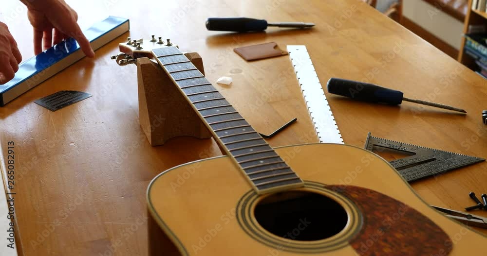Close up hands of a luthier sanding and leveling the frets on an