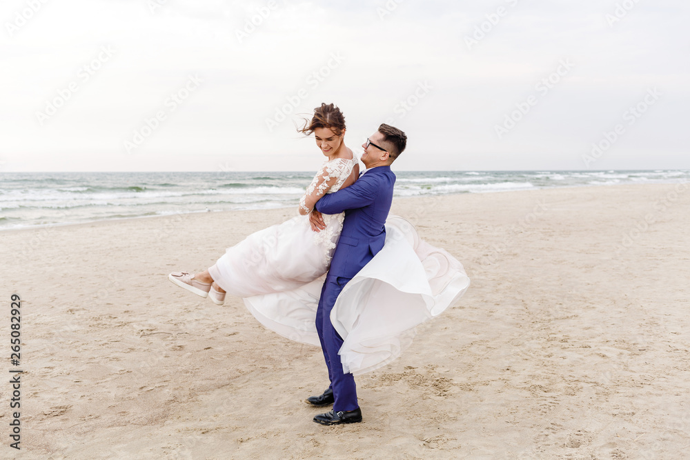 newlyweds walking along the sea beach at the wedding. The groom hugs the bride newlyweds walking along the sea beach at the wedding. The groom hugs the bride