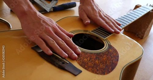 Close up hands of a luthier craftsman measuring and leveling an acoustic guitar neck fretboard on a wood workshop bench with lutherie tools. photo