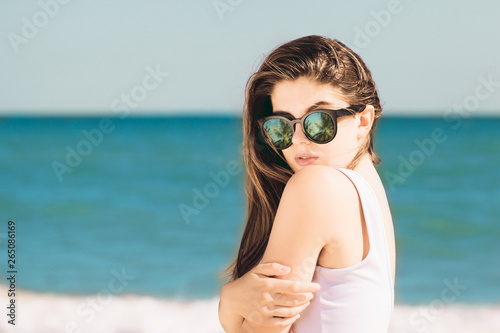 Portrait of a pretty girl with long hair in trendy sunglasses with palms reflection posing on the beach