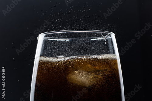 Glass of pouring fizzy drink with ice on a black background