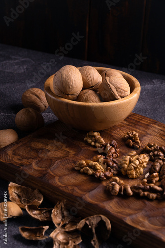 Walnuts in wooden bowl on wooden carved board, side view. Healthy nuts and seeds composition. photo