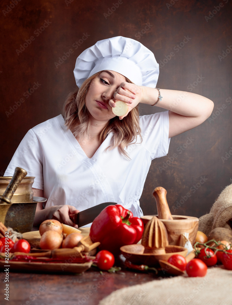 Young woman in a chef uniform cuts onions and cries. Young woman in a chef uniform cuts onions and cries.