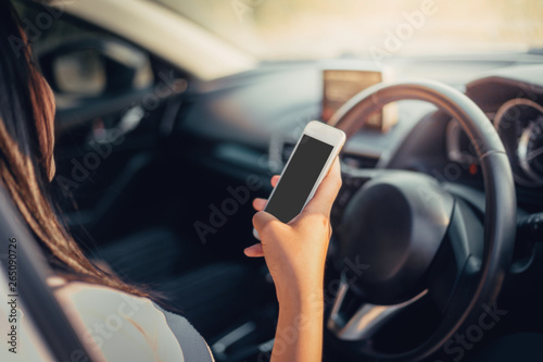 Young woman driving the car and use the phone while driving. sun shines through front window. sun shines through front window. Blurred background and Soft focus.