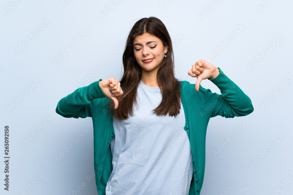 Teenager girl over blue wall showing thumb down Teenager girl over blue wall showing thumb down