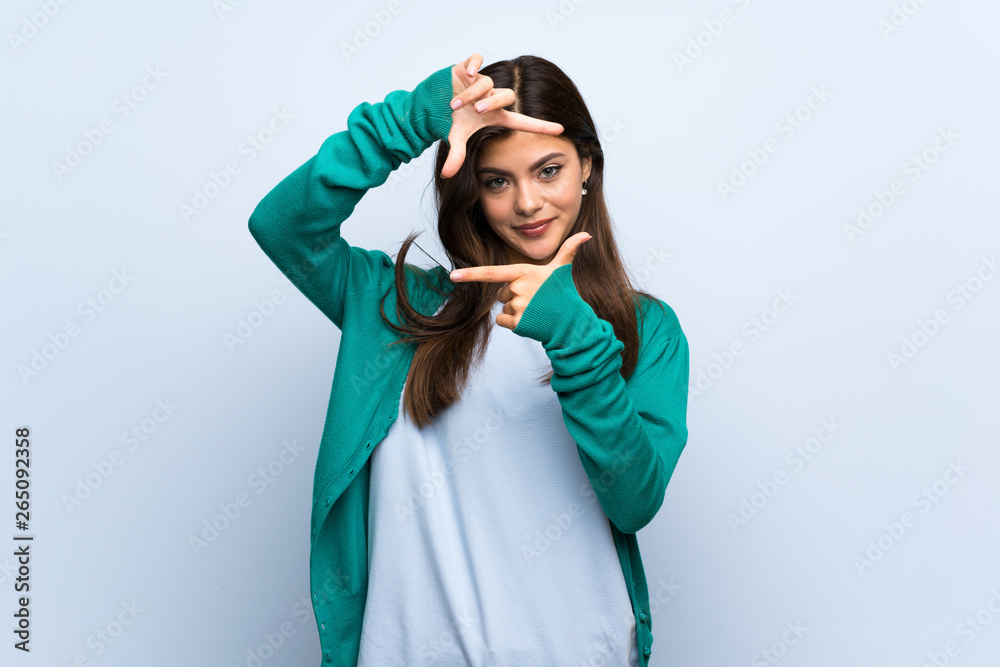Teenager girl over blue wall focusing face. Framing symbol Teenager girl over blue wall focusing face. Framing symbol