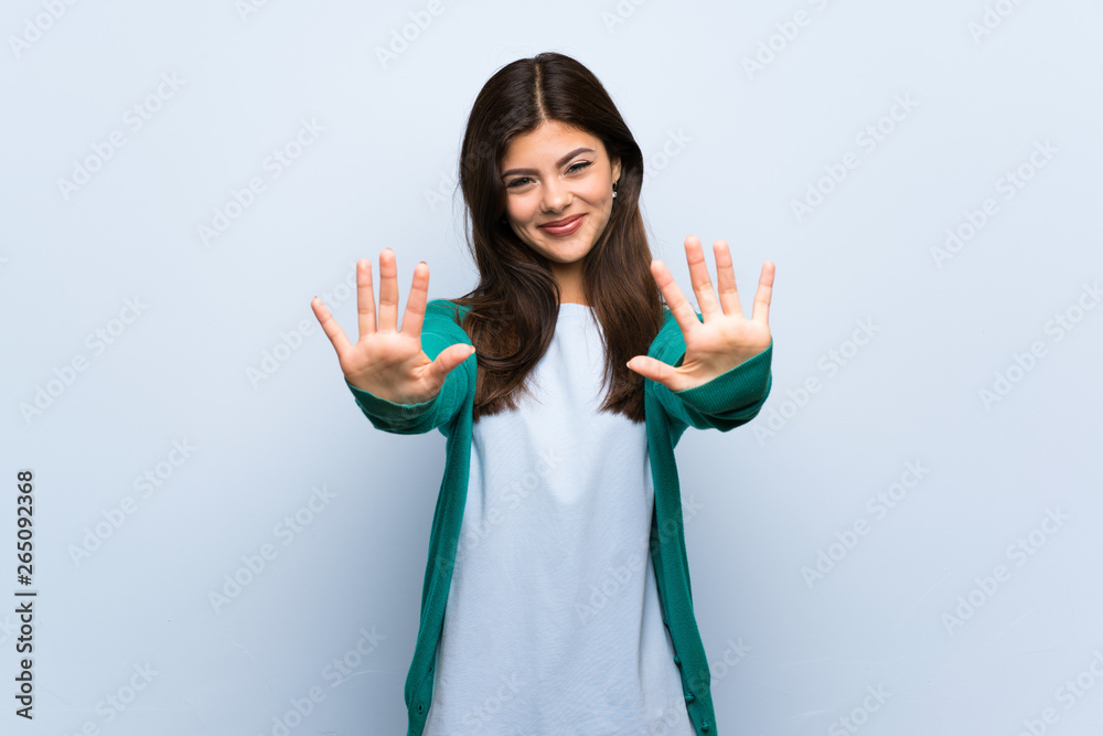 Teenager girl over blue wall counting ten with fingers Teenager girl over blue wall counting ten with fingers