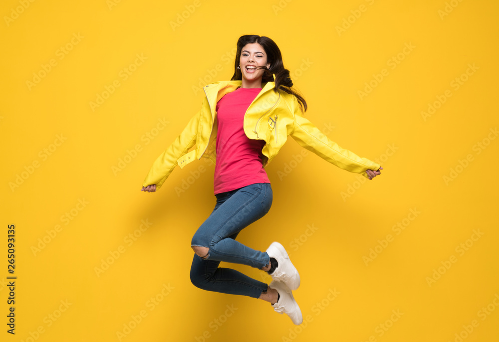 Teenager girl jumping over isolated yellow wall