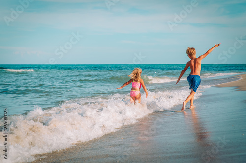 little girl and boy run fly play with waves on beach