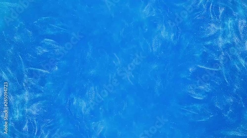 Abstract Waves of blue pearl paint in water top view.