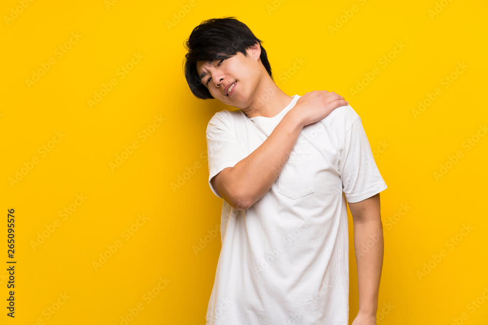 Asian man over isolated yellow wall suffering from pain in shoulder for having made an effort Asian man over isolated yellow wall suffering from pain in shoulder for having made an effort