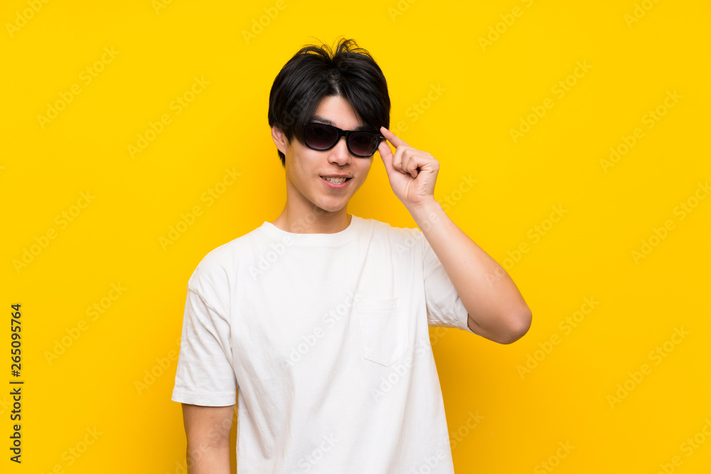 Asian man over isolated yellow wall with glasses and surprised Asian man over isolated yellow wall with glasses and surprised
