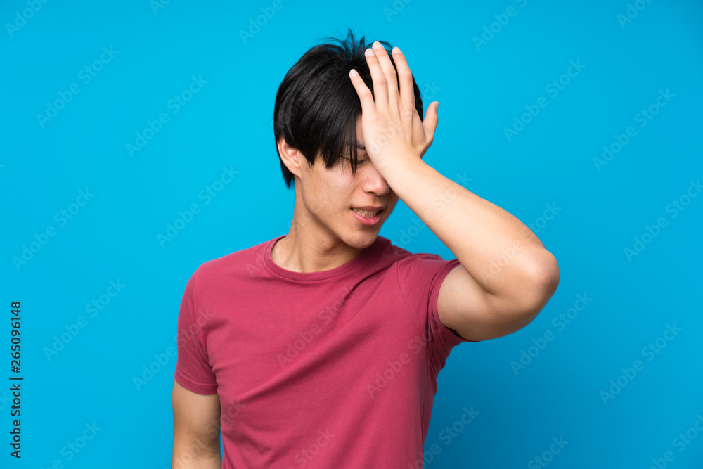 Asian man with red shirt over isolated blue wall having doubts with confuse face expression Asian man with red shirt over isolated blue wall having doubts with confuse face expression