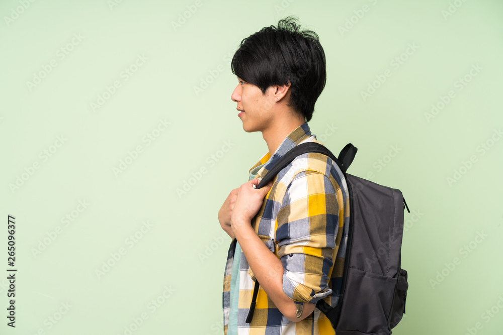 Asian man over isolated green wall with backpack Asian man over isolated green wall with backpack