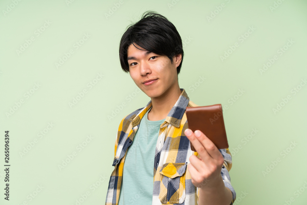 Asian man over isolated green wall holding a wallet Asian man over isolated green wall holding a wallet