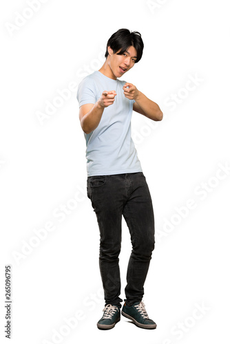 A full-length shot of a Asian man with blue shirt pointing to the front and smiling over isolated white background © luismolinero
