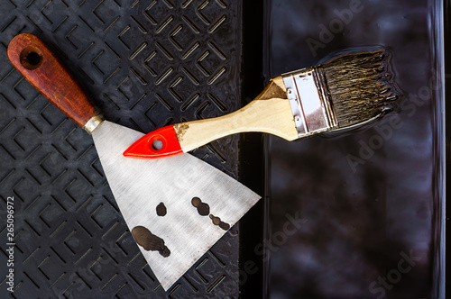 Close up of a wooden brush and a shpatel laying in a black roller tray with stains of brown paint photo