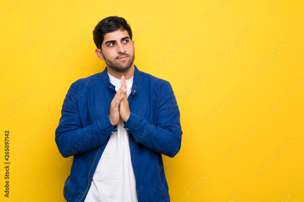 Man with blue jacket over yellow wall scheming something Man with blue jacket over yellow wall scheming something